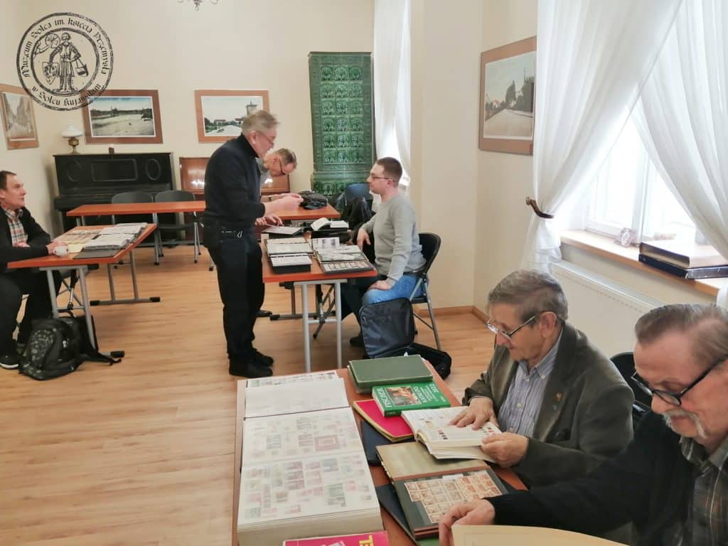 Zdjęcie przedstawiające uczestników Klubu Kolekcjonera w dniu 31.03.2023 r. Na pierwszym planie filateliści przeglądający swoje zbiory. Na dalszym planie rozmawiający kolekcjonerzy.