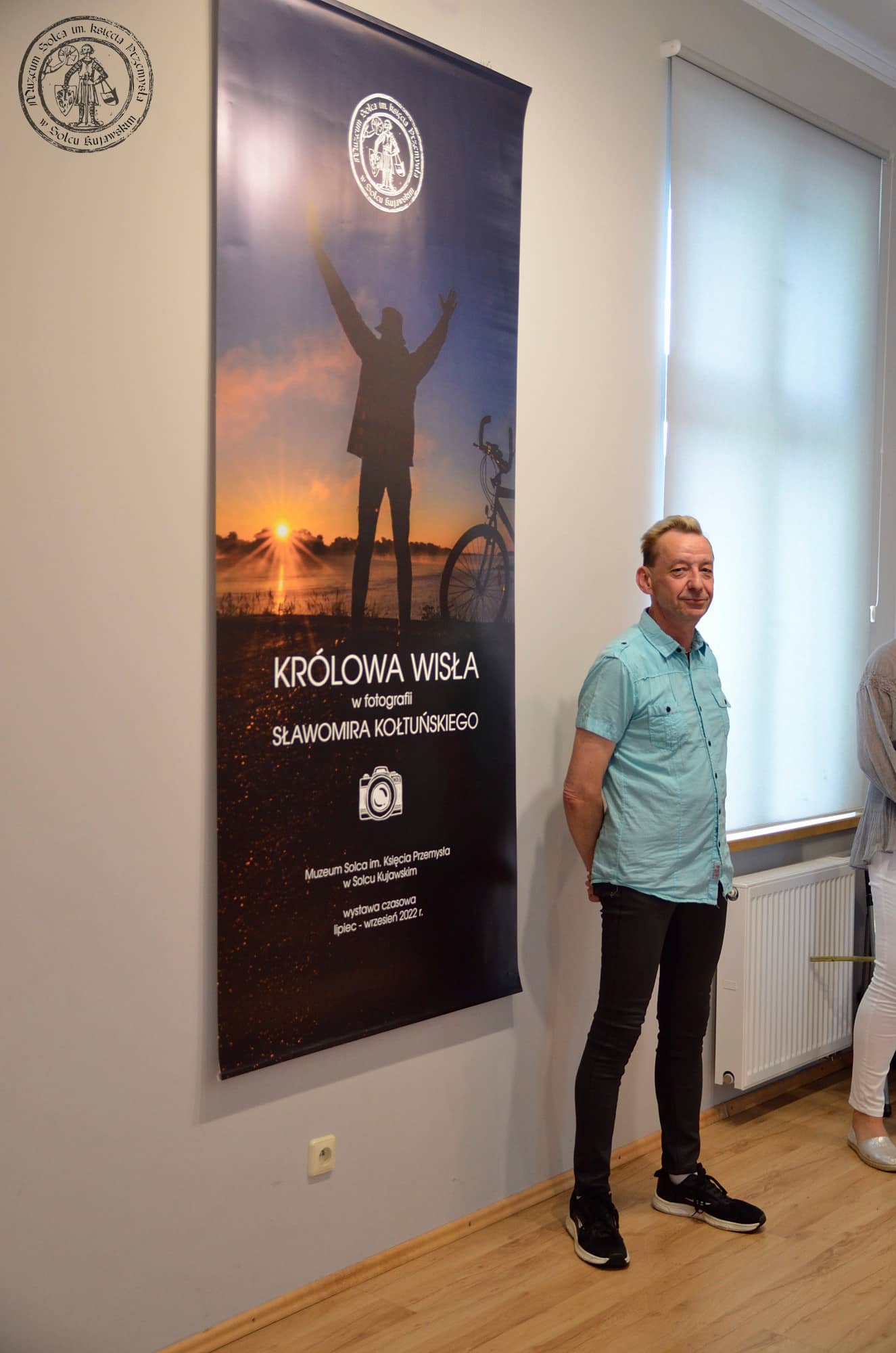 Sławomir Kołtuński przy planszy tytułowej wystawy "Królowa Wisła w fotografii Sławomira Kołtuńskiego".
