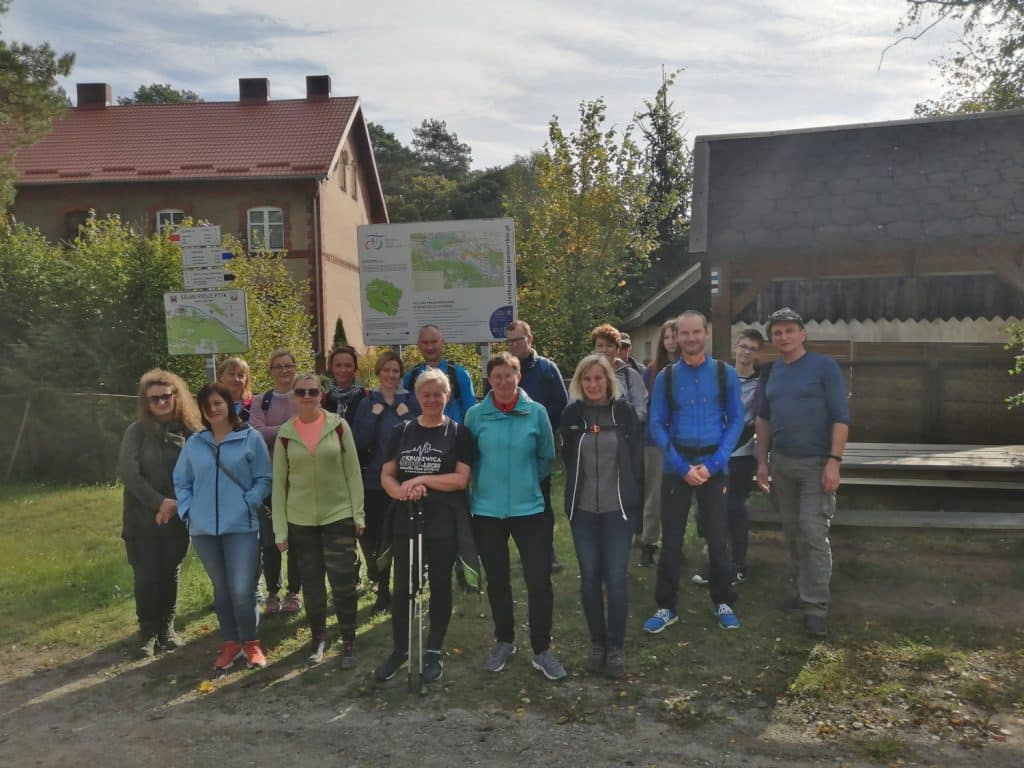 Rajd z Przyłubia do Solca Kujawskiego (08.10.2022 r.) - Zdjęcie grupowe przy tablicy informacyjnej o szlakach przy dworcu PKP w Przyłubiu. - Zdjęcie 2