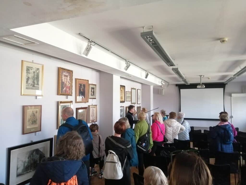 Zdjęcie przedstawia grupę osób oglądających zbiory muzealne.